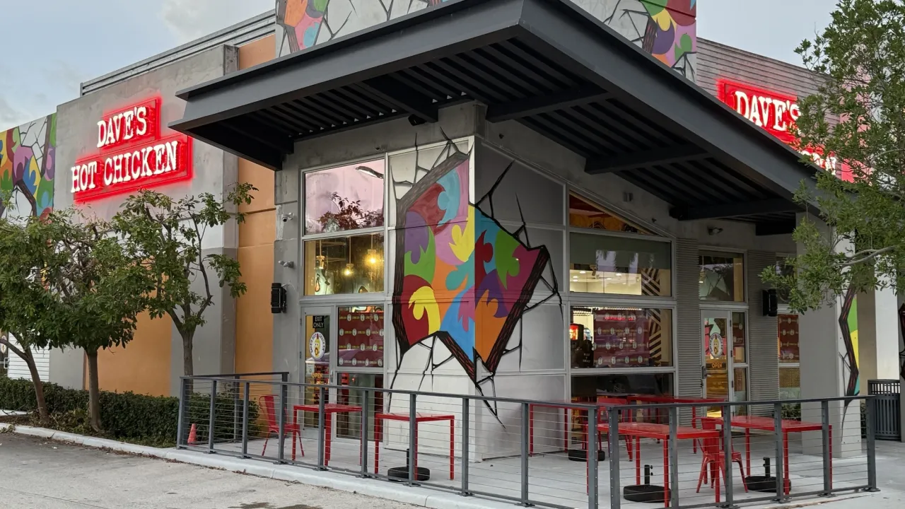 Exterior view of Dave's Hot Chicken at 2390 N Federal Hwy, Pompano Beach, FL, showcasing vibrant murals and red seating.