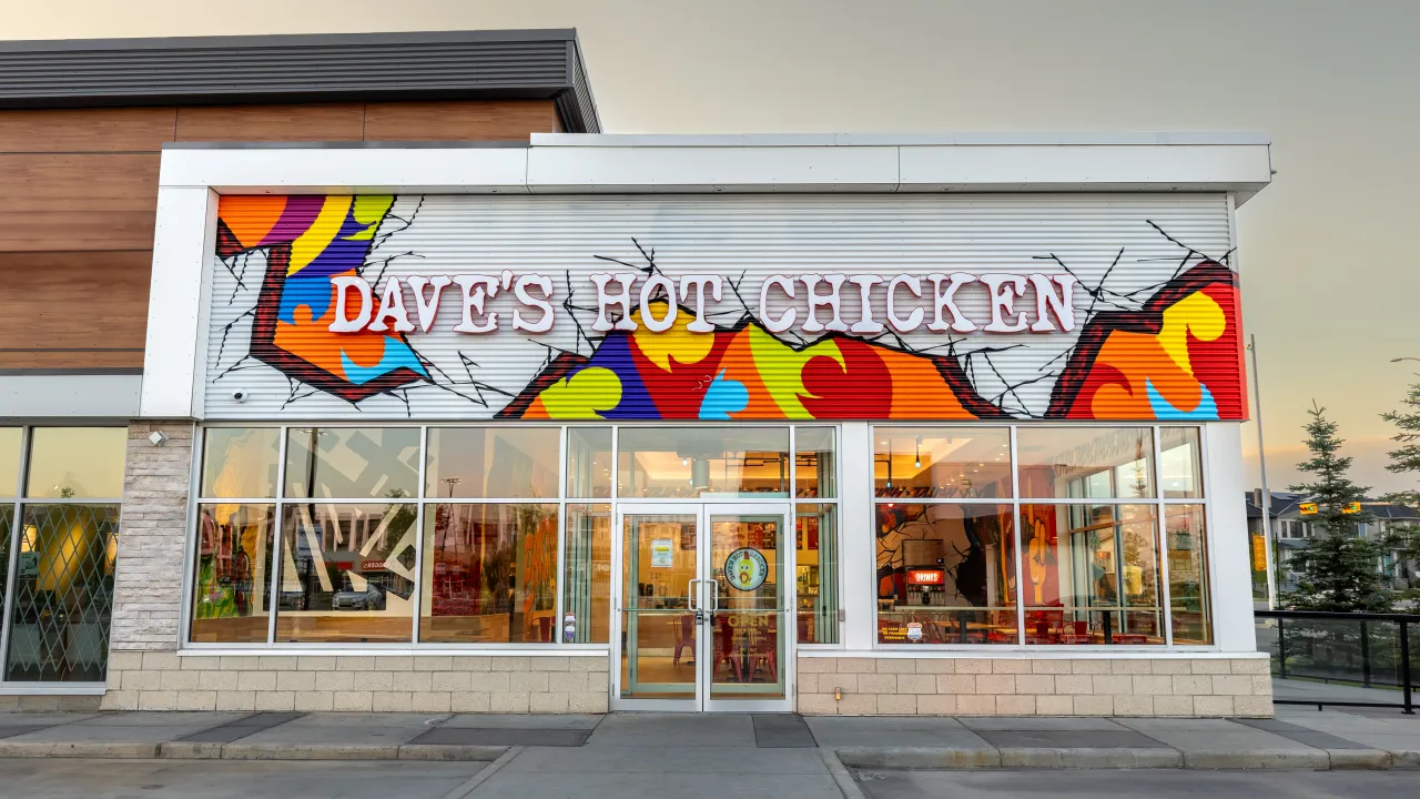 Exterior view of Dave's Hot Chicken at 409 E. Hills Blvd. SE #215, Calgary, AB, showcasing vibrant mural and welcoming entrance.
