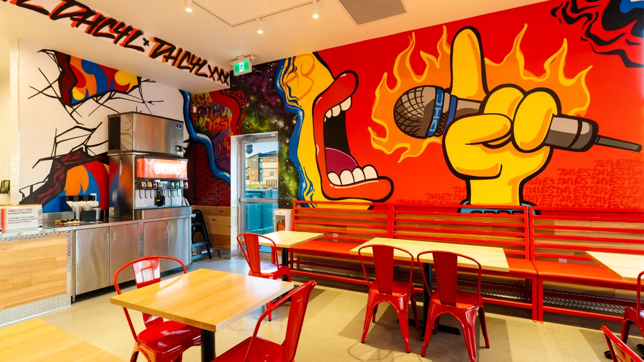 Interior view of Dave's Hot Chicken at 409 E. Hills Blvd. SE #215, Calgary, AB, showcasing vibrant murals and red furniture.