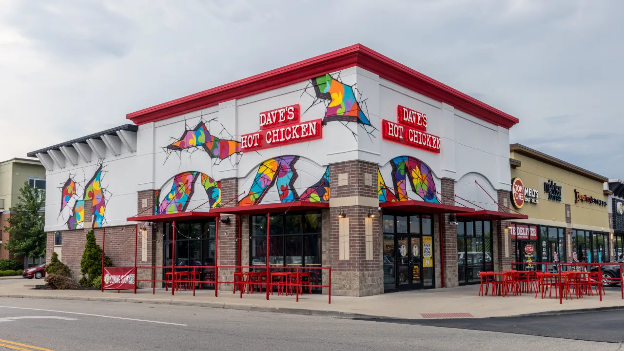 Exterior view of Dave's Hot Chicken at 3208 Vandercar Way, Cincinnati, OH, showcasing vibrant murals and red outdoor seating.