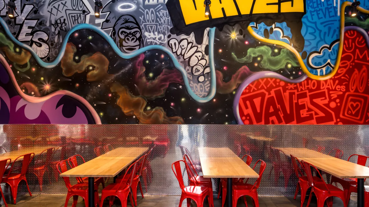 Interior view of Dave's Hot Chicken at 3208 Vandercar Way, Cincinnati, OH, showcasing colorful murals and red chairs.