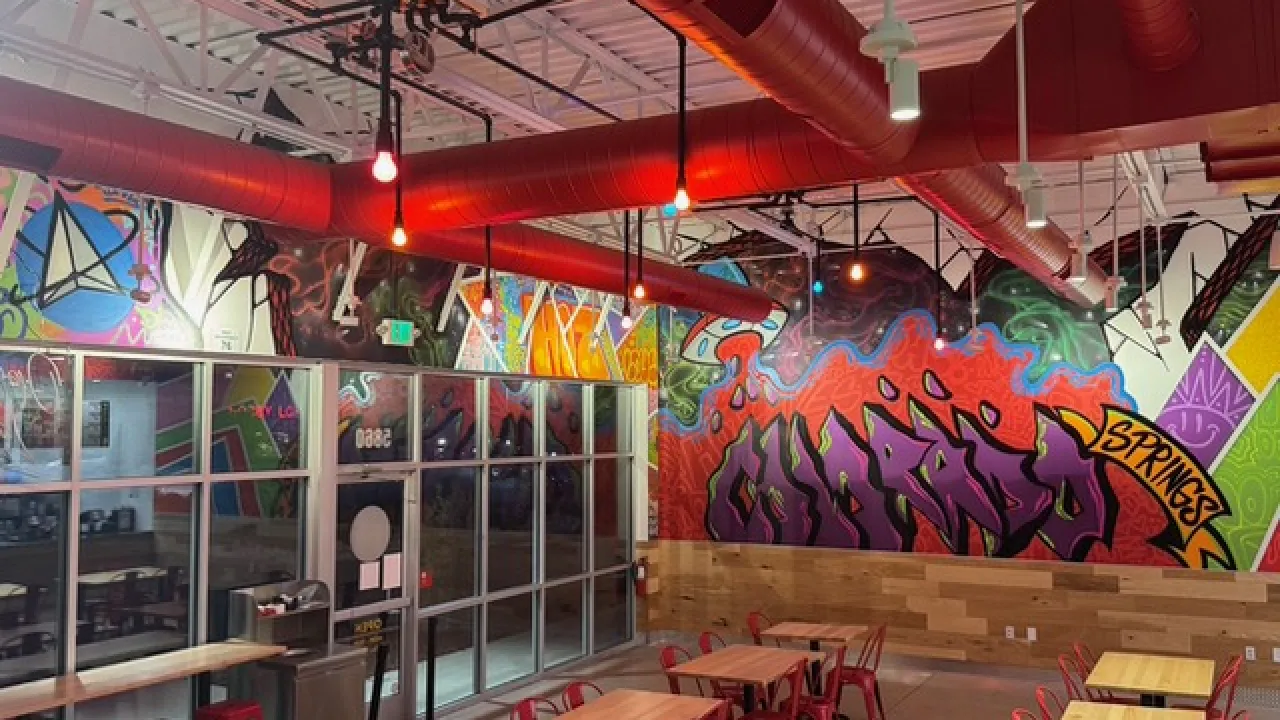 Interior view of Dave's Hot Chicken on Barnes Rd, Colorado Springs, CO, showcasing vibrant murals and casual dining furniture.
