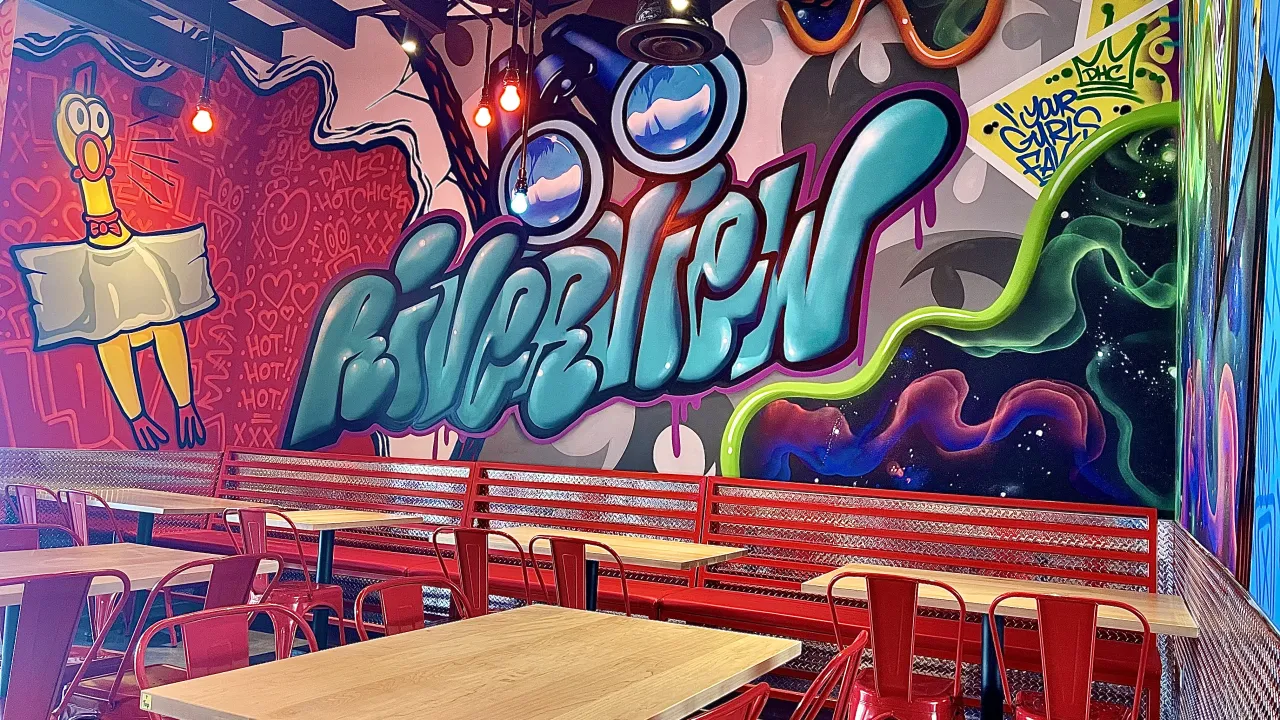 Interior view of Dave's Hot Chicken on Big Bend Road, Riverview, FL, showcasing vibrant murals and red seating.