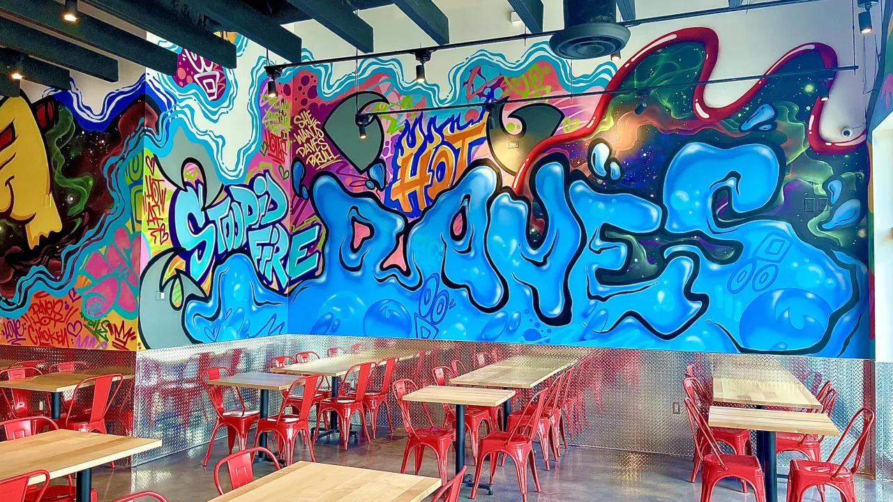 Interior view of Dave's Hot Chicken on Big Bend Road, Riverview, FL, featuring vibrant graffiti and red metal chairs.