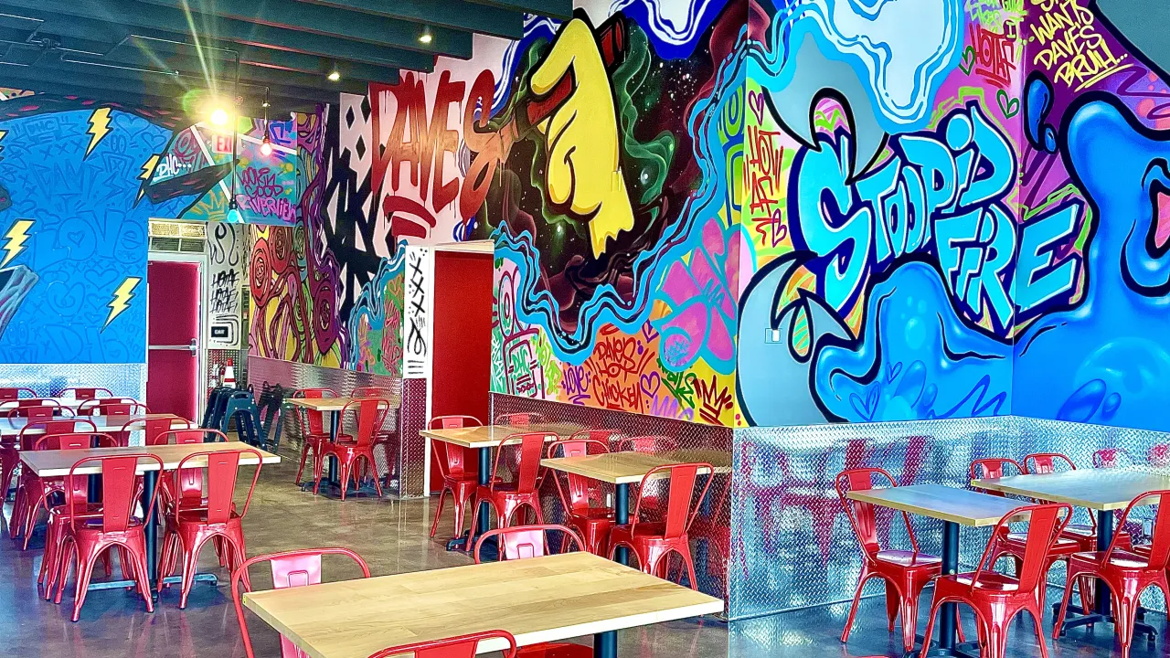 Interior view of Dave's Hot Chicken on Big Bend Road, Riverview, FL, showcasing vibrant murals and red metal seating.