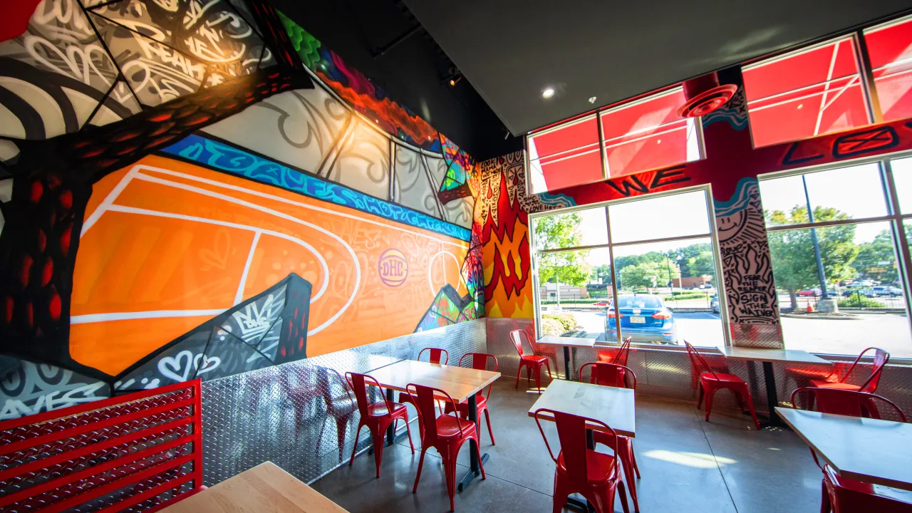 Interior view of Dave's Hot Chicken on Cobb Pkwy NW, Kennesaw, GA, showcasing vibrant murals and red metal chairs.