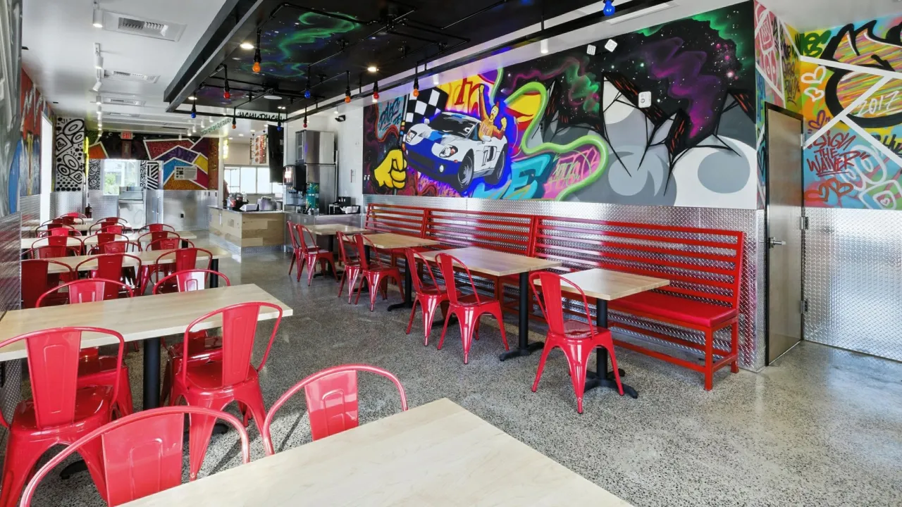 Interior view of Dave's Hot Chicken at 318 North Dupont Hwy, Dover, DE, featuring vibrant murals and red seating.