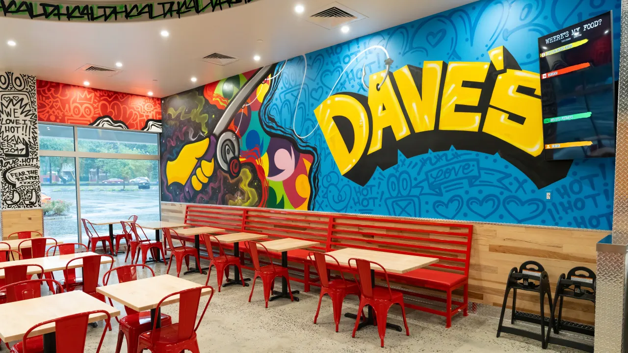 Interior view of Dave's Hot Chicken on NJ-70 W, Brick, NJ, showcasing vibrant murals and red seating.