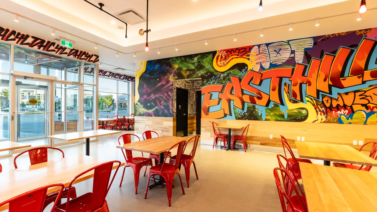 Interior view of Dave’s Hot Chicken on Sarcee Trail NW, Calgary, AB, showcasing vibrant graffiti and wooden tables.
