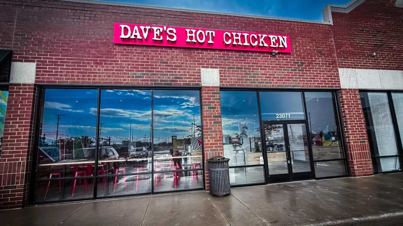 Exterior view of Dave's Hot Chicken on Allen Road, Woodhaven, MI, showcasing red signage and modern glass windows.