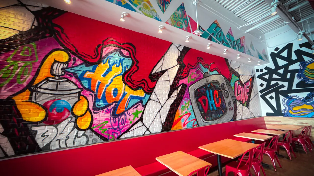 Interior view of Dave's Hot Chicken on Allen Road, Woodhaven, MI, showcasing vibrant murals and red seating.