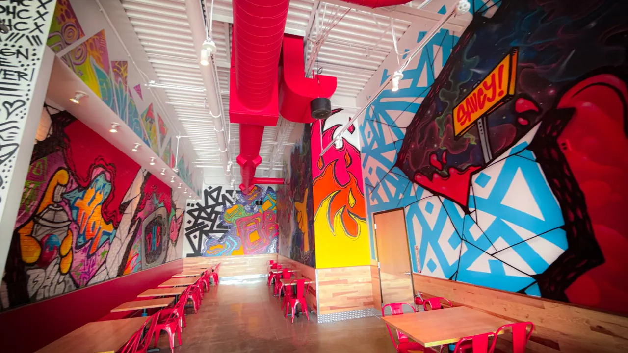 Interior view of Dave's Hot Chicken on Allen Road, Woodhaven, MI, showcasing vibrant murals and modern red seating.