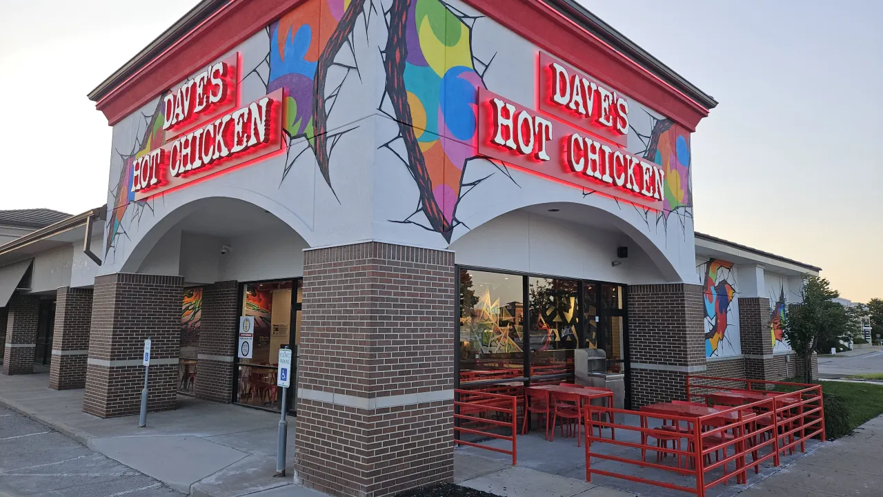 Exterior view of Dave's Hot Chicken on Chipman Rd, Lee's Summit, MO, showcasing vibrant murals and red patio seating.
