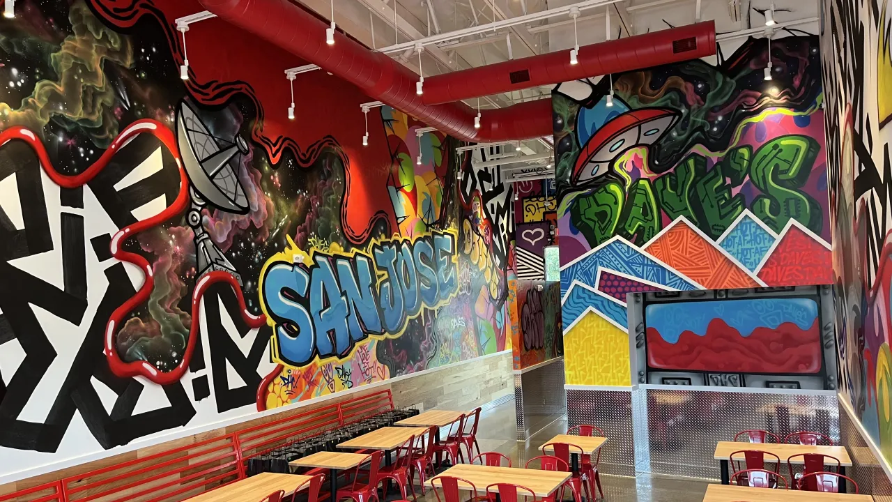 Interior view of Dave's Hot Chicken on Cottle Road, San Jose, CA, showcasing vibrant murals and modern seating.