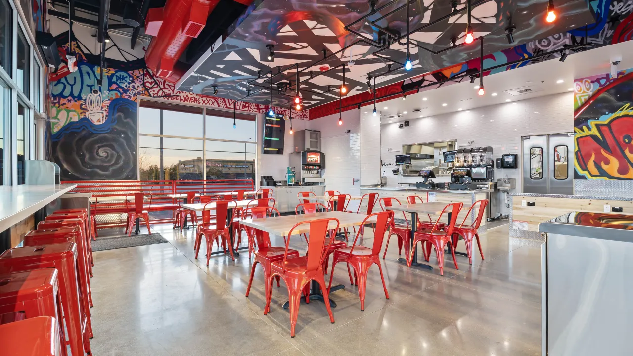 Interior view of Dave’s Hot Chicken on Greenbrier Dr, Normal, IL, featuring vibrant murals and red metal seating.
