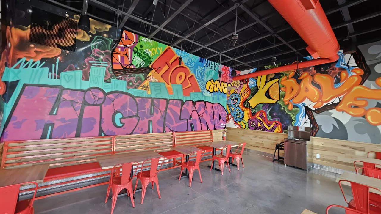 Interior view of Dave's Hot Chicken on Greenspot Rd, Highland, CA, showcasing vibrant murals and red metal seating.
