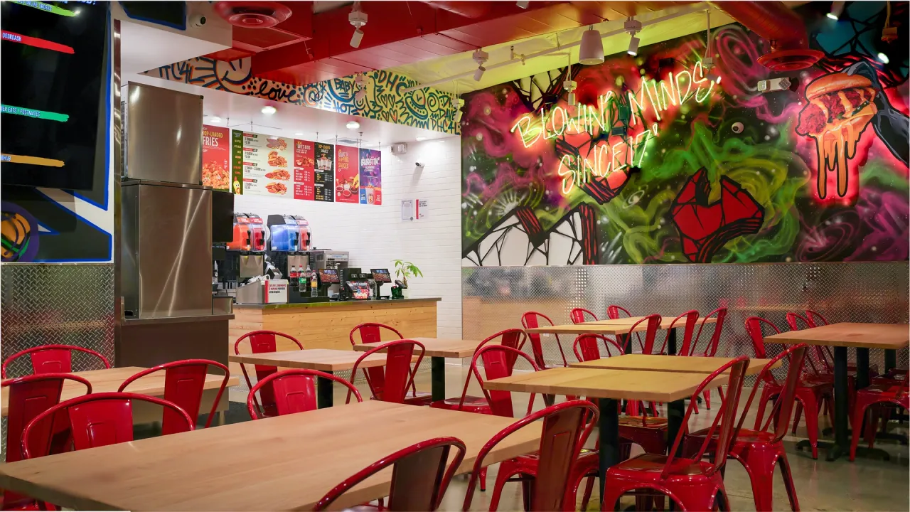 Interior view of Dave's Hot Chicken at 865 South Indian Hill Blvd, Claremont, CA, featuring vibrant murals and red seating.