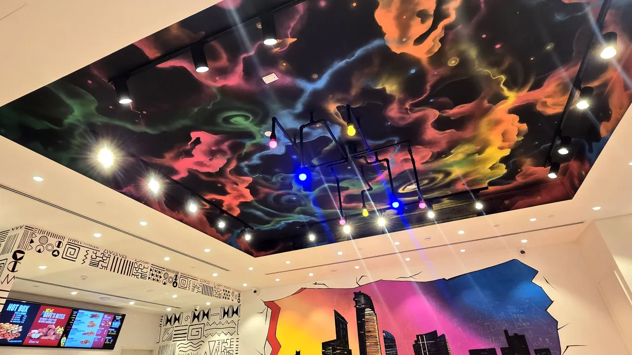 Interior view of Dave’s Hot Chicken on King Salman Bin Abdulaziz Al Saud Street, Abu Dhabi, featuring a vibrant ceiling mural and colorful pendant lights.