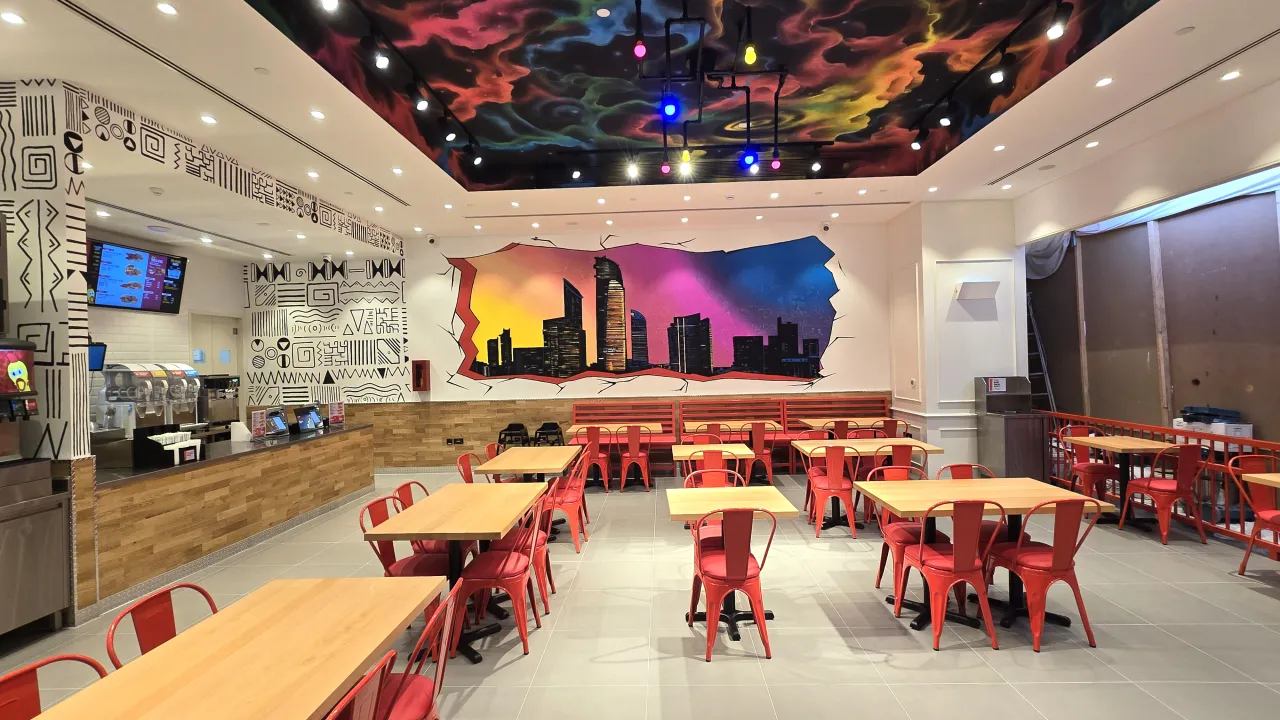 Interior view of Dave’s Hot Chicken on King Salman Bin Abdulaziz Al Saud Street, Abu Dhabi, featuring vibrant wall art and red chairs.
