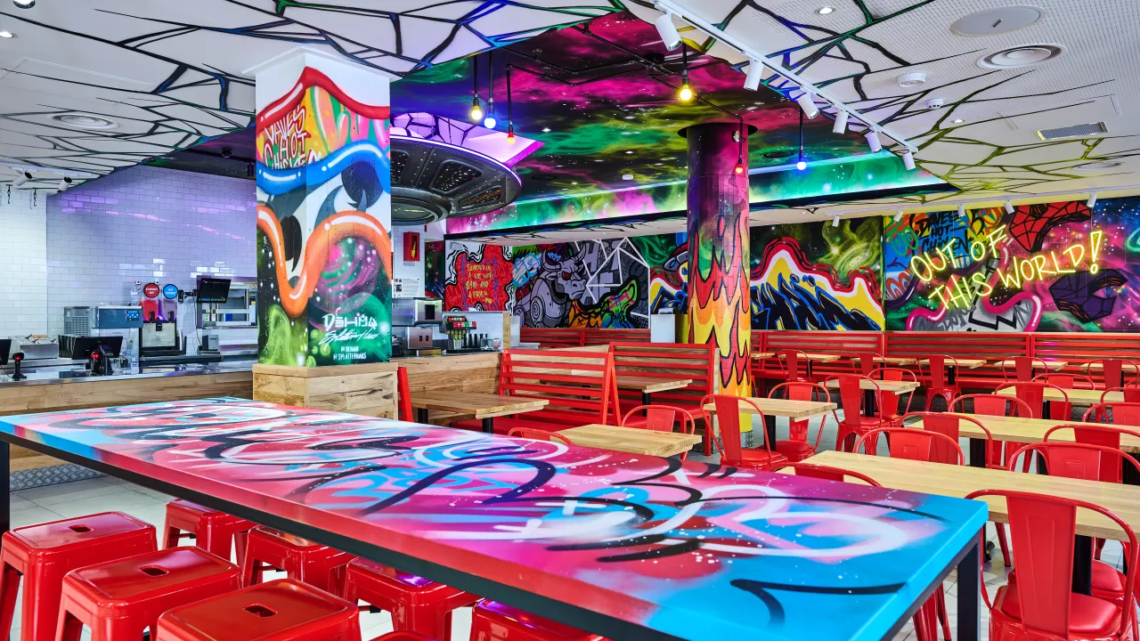 Interior view of Dave's Hot Chicken at 56 New Street, Birmingham, England, showcasing vibrant murals and red seating.