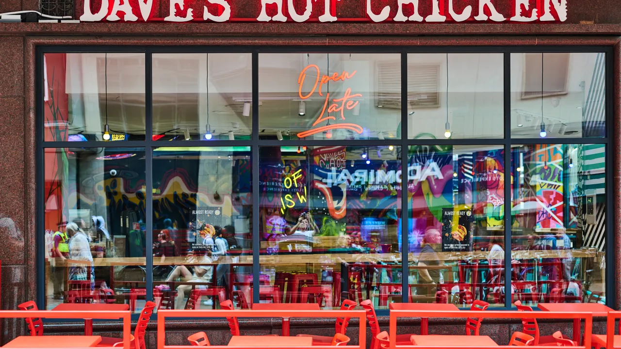 Exterior view of Dave's Hot Chicken on 56 New Street, Birmingham, England, showcasing vibrant red signage and outdoor seating.