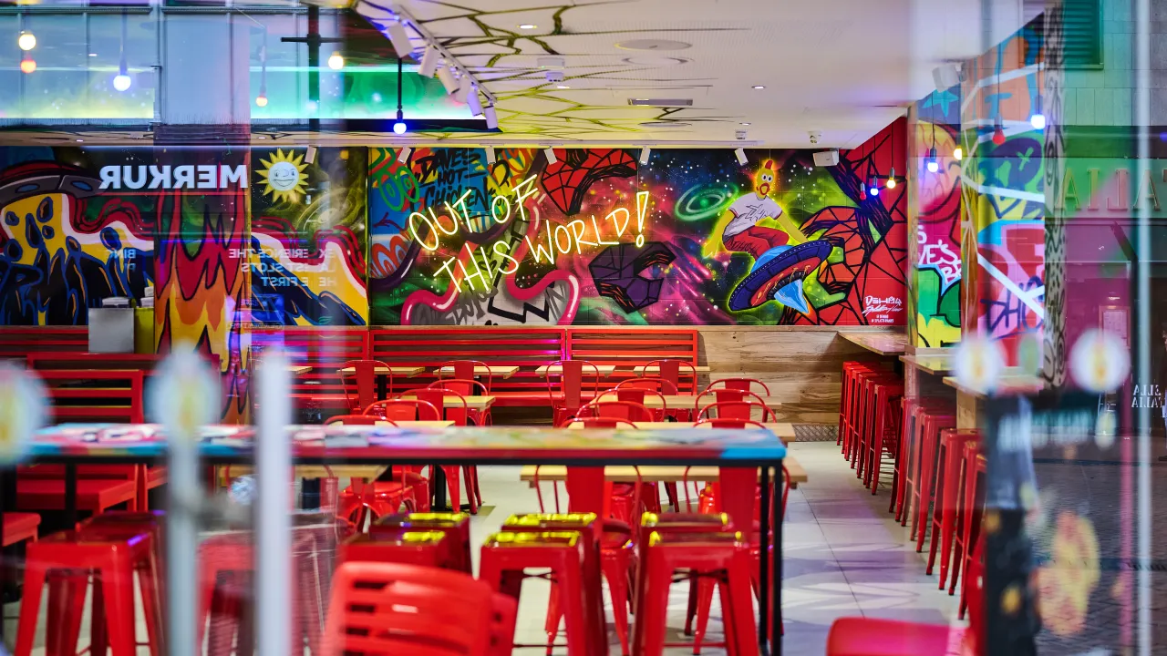 Interior view of Dave's Hot Chicken on 56 New Street, Birmingham, England, showcasing vibrant murals and red seating.