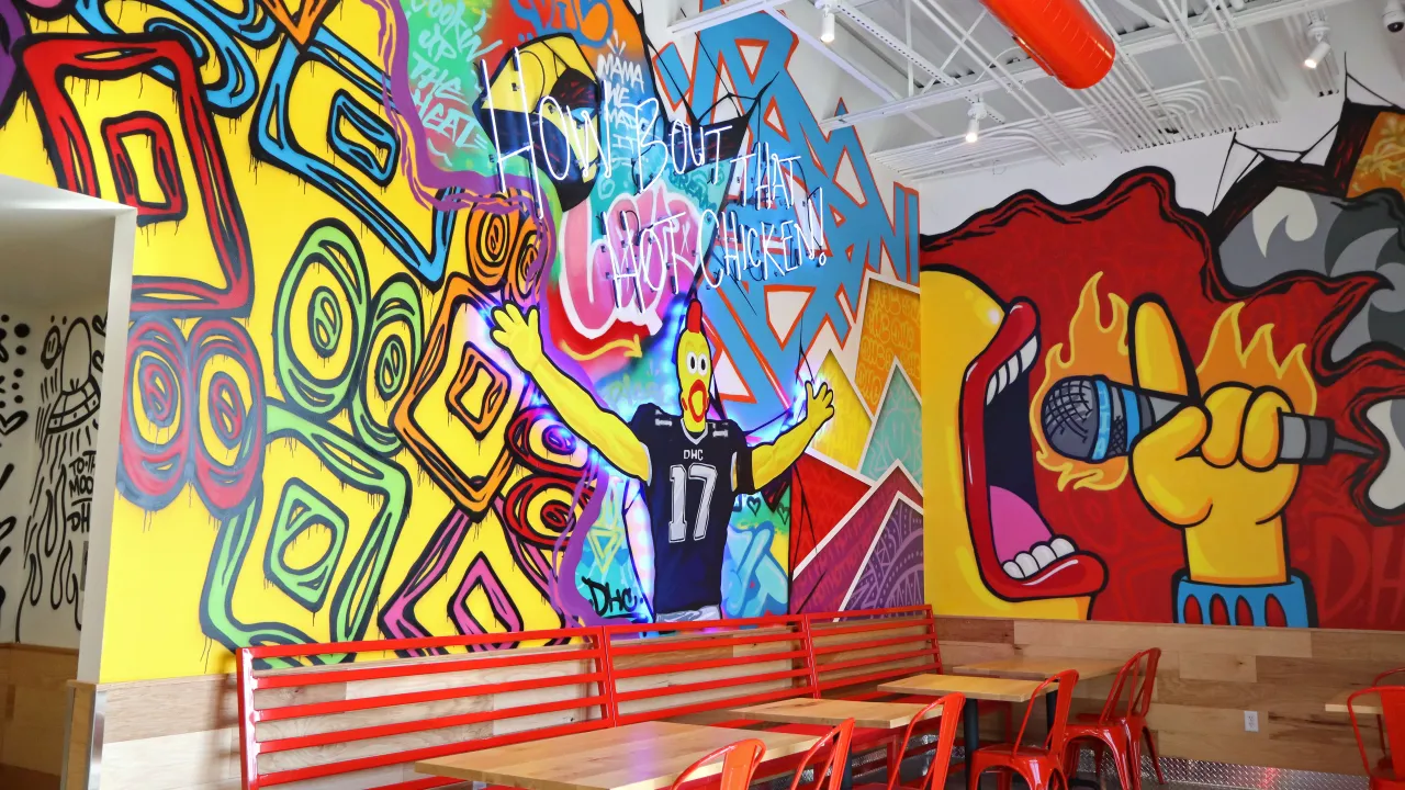 Interior view of Dave's Hot Chicken on North Main St, Logan, UT, showcasing vibrant murals and red seating.