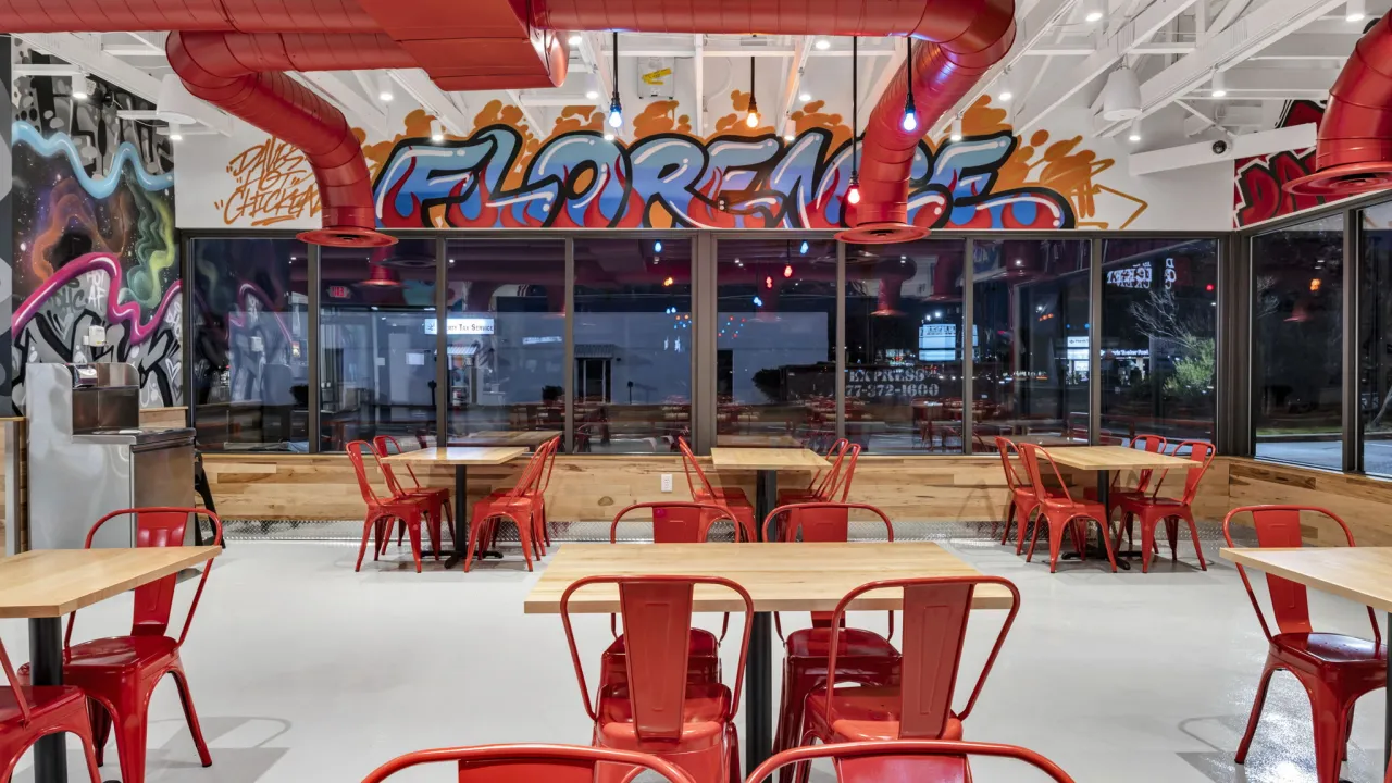 Interior view of Dave's Hot Chicken on W. Palmetto St, Florence, SC, featuring vibrant murals and red metal seating.