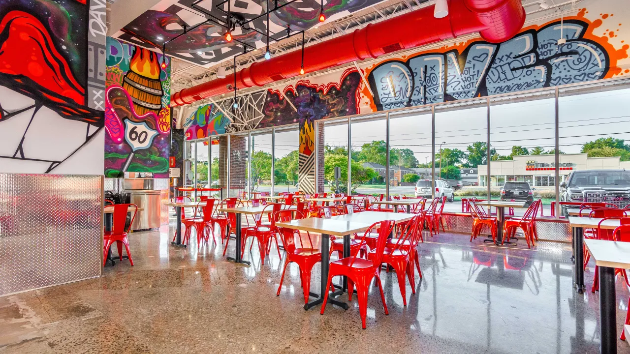 Interior view of Dave's Hot Chicken on Shelbyville Road, Louisville, KY, showcasing vibrant murals and red seating.
