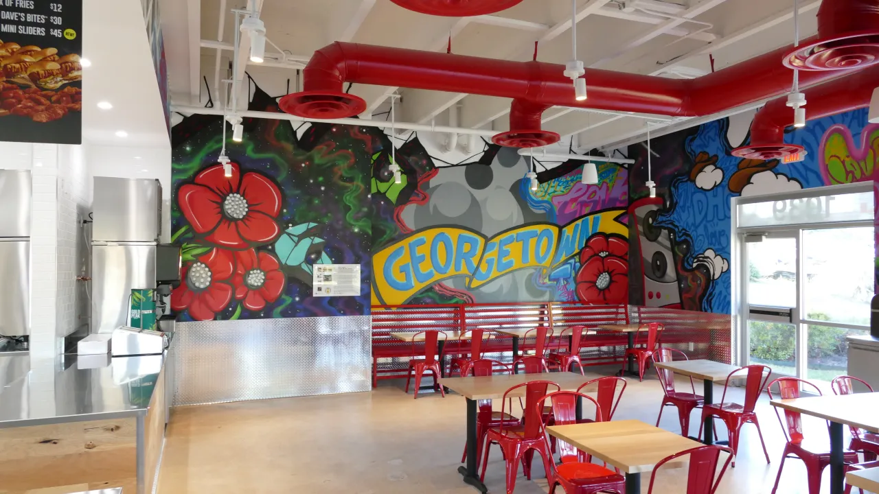 Interior view of Dave's Hot Chicken on W. University Ave, Georgetown, TX, showcasing vibrant murals and red seating.