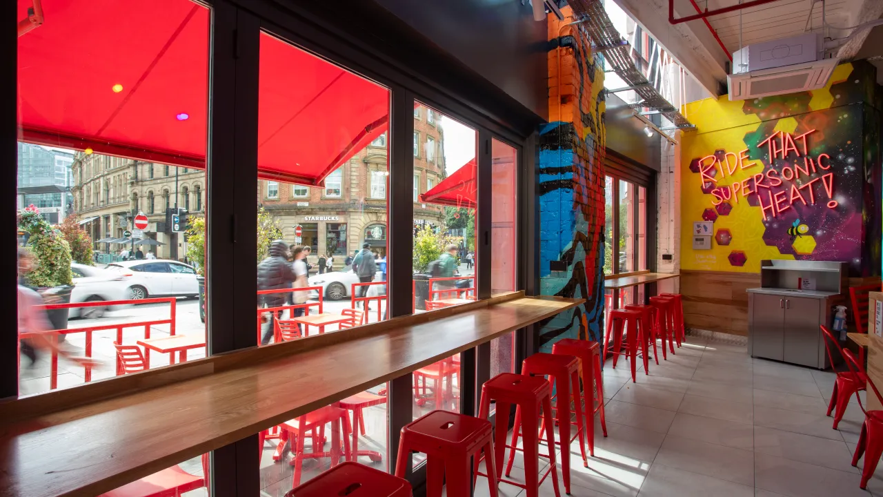 Interior view of Dave's Hot Chicken at 27 Withy Grove, Manchester, M4 2BS, showcasing vibrant murals and red seating.