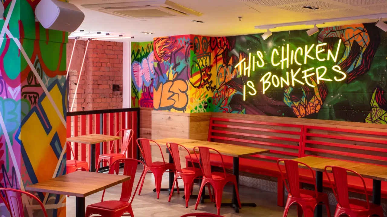Interior view of Dave's Hot Chicken at 27 Withy Grove, Manchester, featuring vibrant murals and red seating.