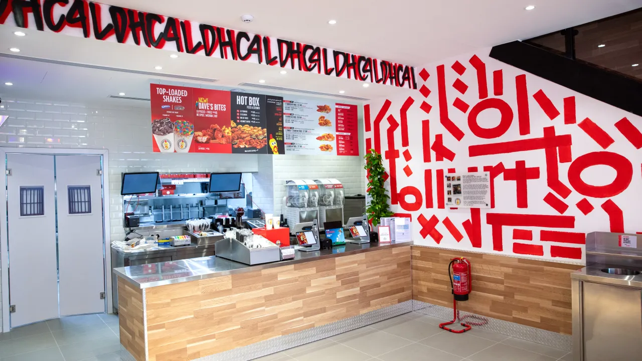 Interior view of Dave's Hot Chicken on Anas Ibn Malik Rd, Riyadh, Saudi Arabia, showcasing vibrant red murals and a modern counter.