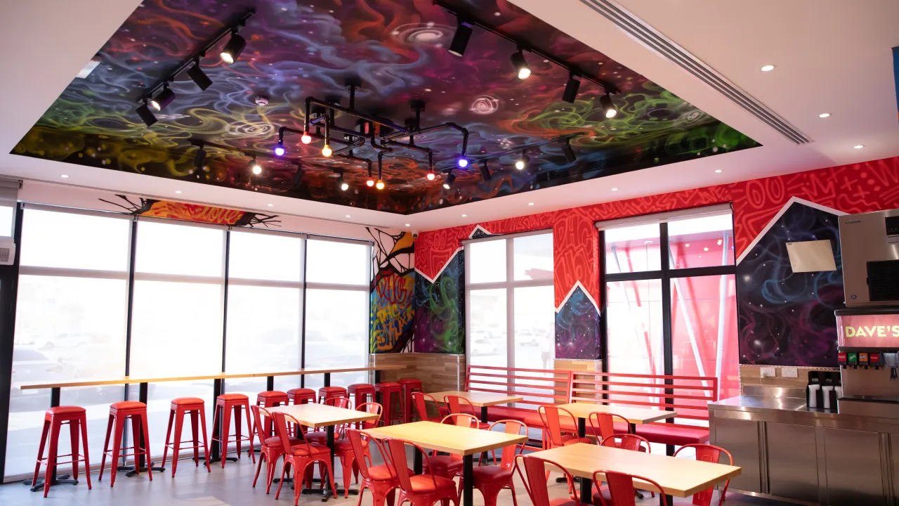 Interior view of Dave's Hot Chicken on Anas Ibn Malik Rd, Riyadh, Saudi Arabia, showcasing vibrant murals and red seating.