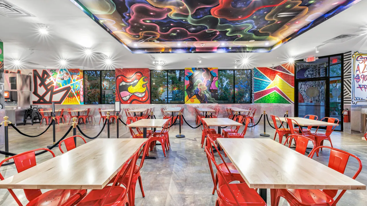 Interior view of Dave's Hot Chicken at 2165 Dixwell Ave, Hamden, CT, showcasing vibrant murals and red seating.