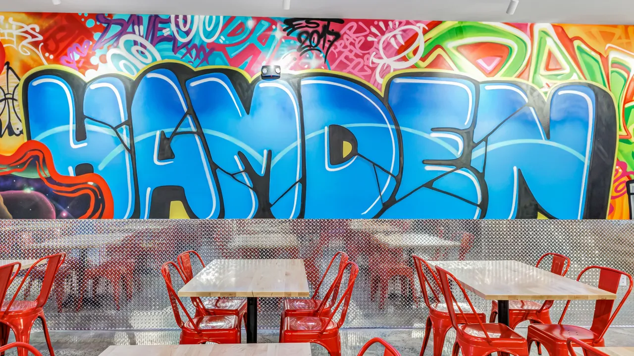 Interior view of Dave’s Hot Chicken on Dixwell Ave, Hamden, CT, showcasing vibrant street art and red chairs.