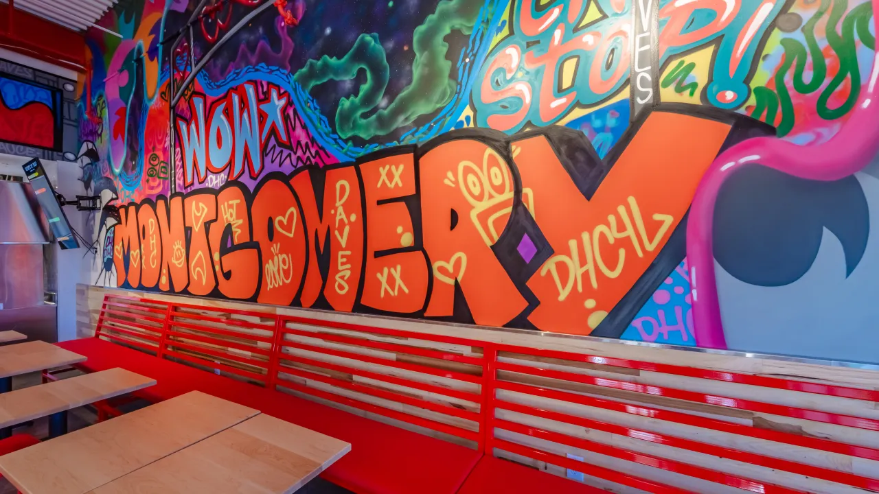Interior view of Dave's Hot Chicken on Eastchase Pkwy, Montgomery, AL, showcasing vibrant murals and red seating.