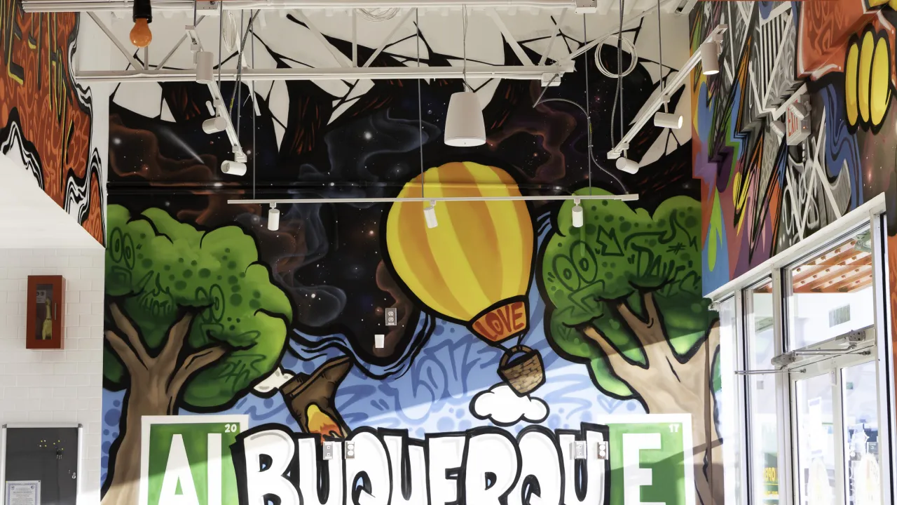 Interior view of Dave's Hot Chicken in Albuquerque, NM, showcasing a vibrant mural with a hot air balloon and lush trees.