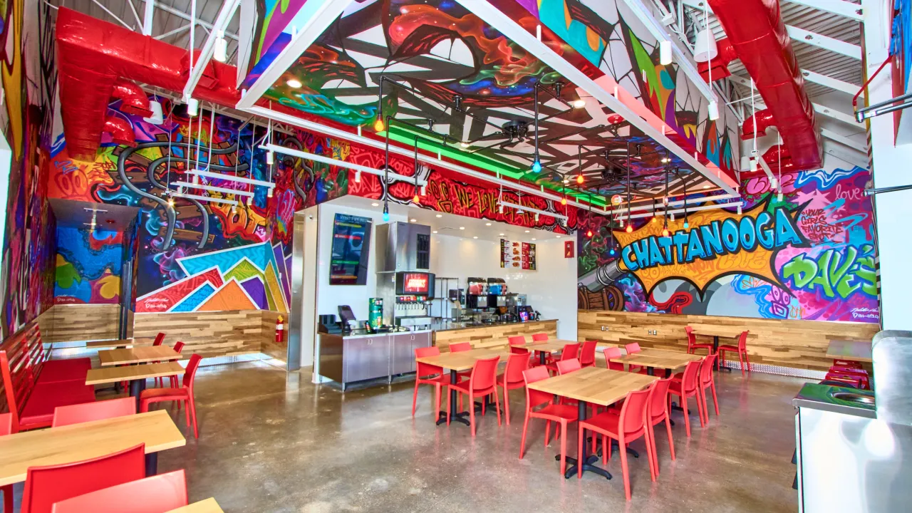 Interior view of Dave's Hot Chicken on Gunbarrel Rd, Chattanooga, TN, showcasing vibrant murals and red seating.