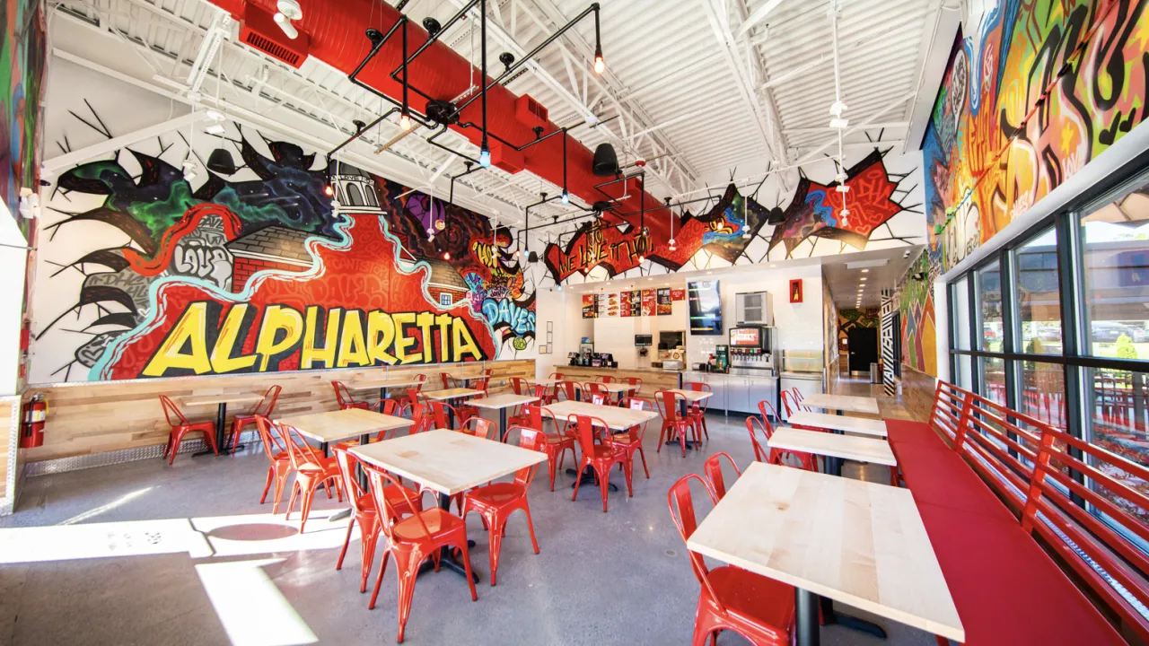 Interior view of Dave's Hot Chicken on Haynes Bridge Rd, Alpharetta, GA, showcasing vibrant murals and red seating.