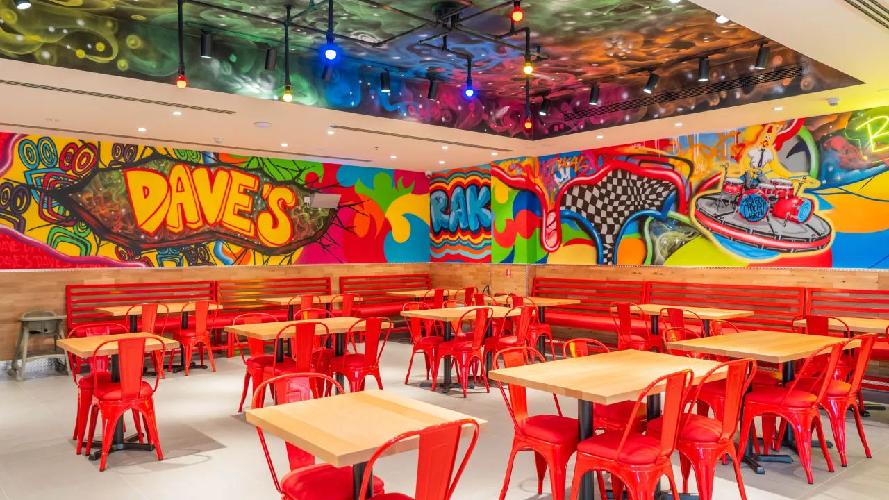 Interior view of Dave's Hot Chicken at Unit GF-AR-04, Al Hamra Mall, Ras Al Khaimah, showcasing vibrant murals and red furniture.