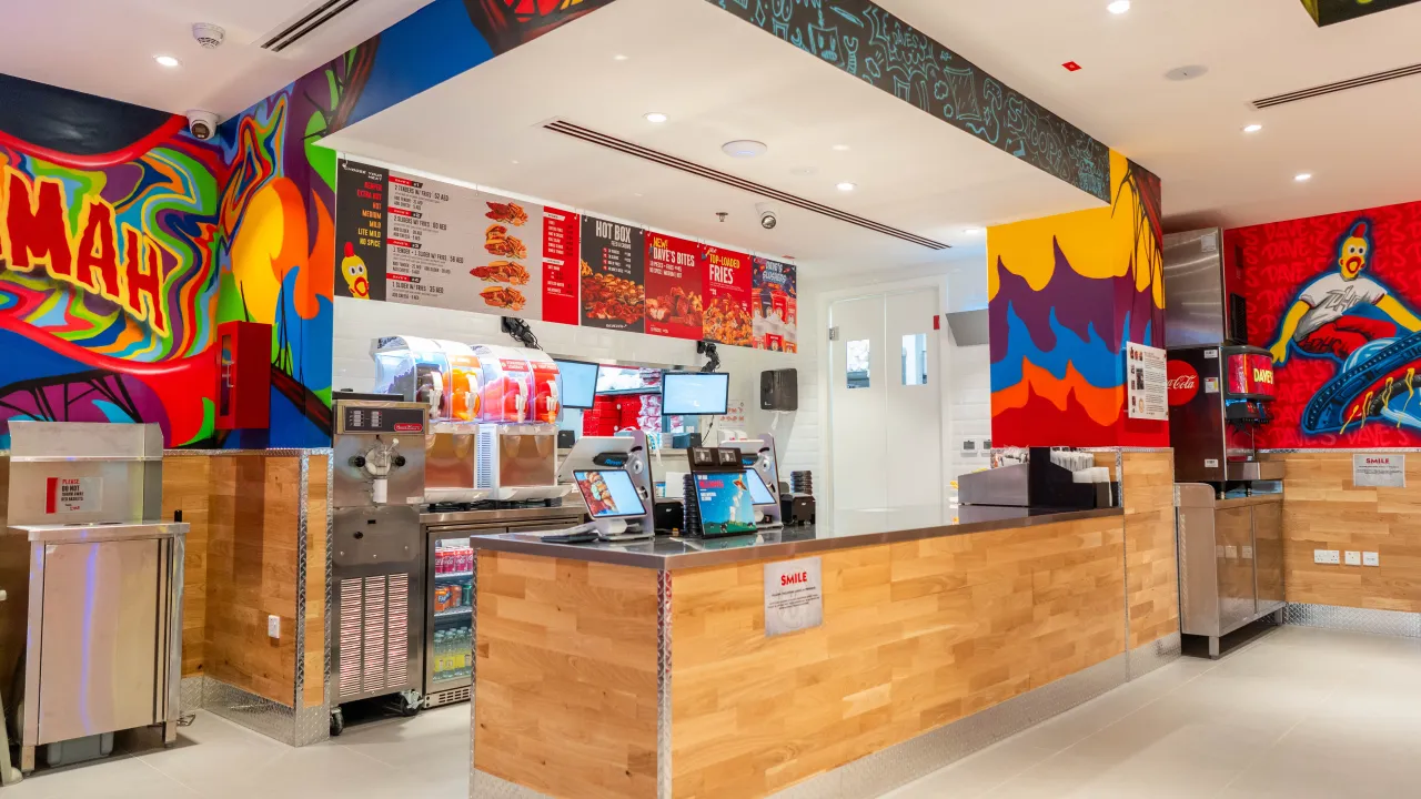 Interior view of Dave's Hot Chicken at Al Hamra Mall, Sheikh Mohamed Bin Salem Road, Ras Al Khaimah, showcasing vibrant murals and a sleek counter.
