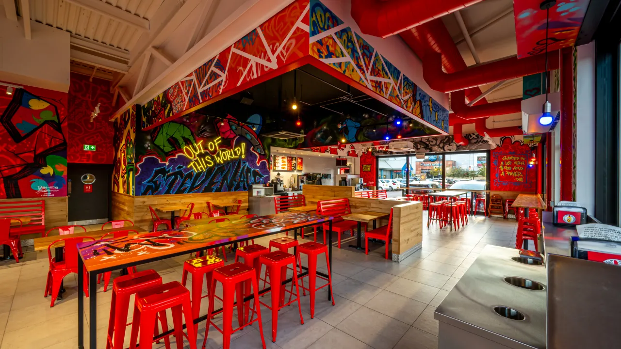 Interior view of Dave's Hot Chicken at Stevenage Leisure Park, Stevenage, UK, showcasing vibrant murals and red seating.