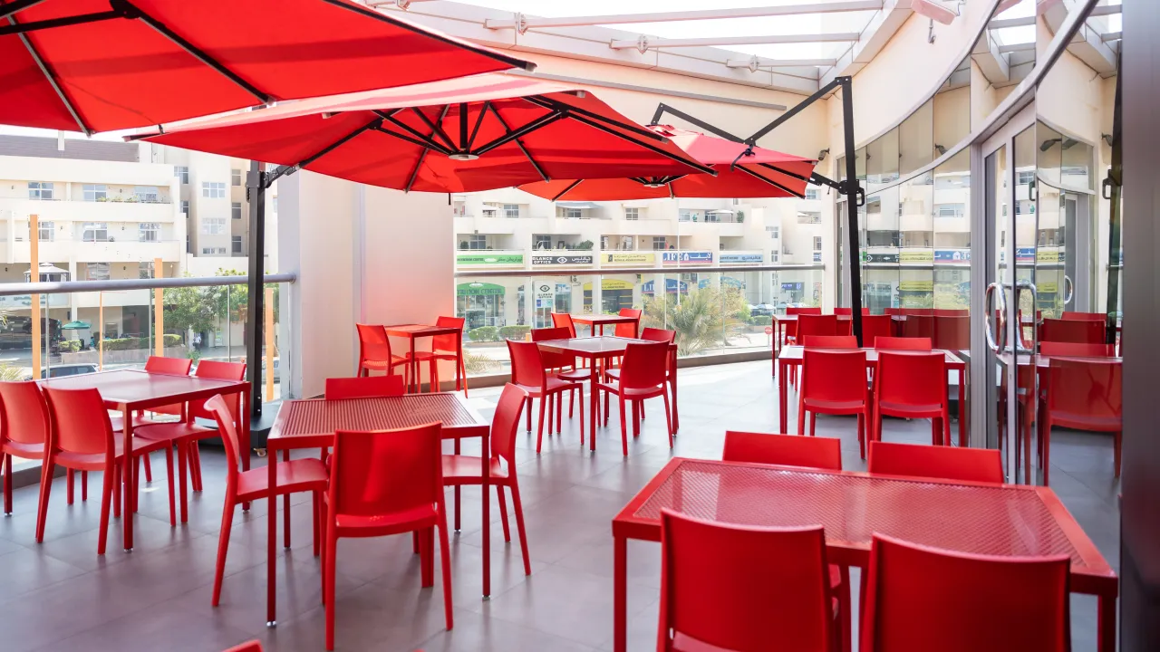 Interior view of Dave's Hot Chicken on Turin Boulevard Road, First Avenue Mall, Dubai, showcasing bright red chairs and umbrellas.