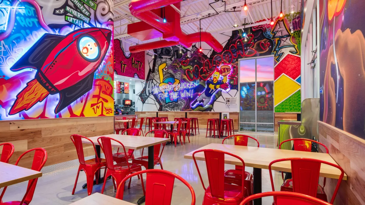 Interior view of Dave's Hot Chicken at 4182 W. 13400 S., Riverton, UT, showcasing vibrant murals and red metal chairs.