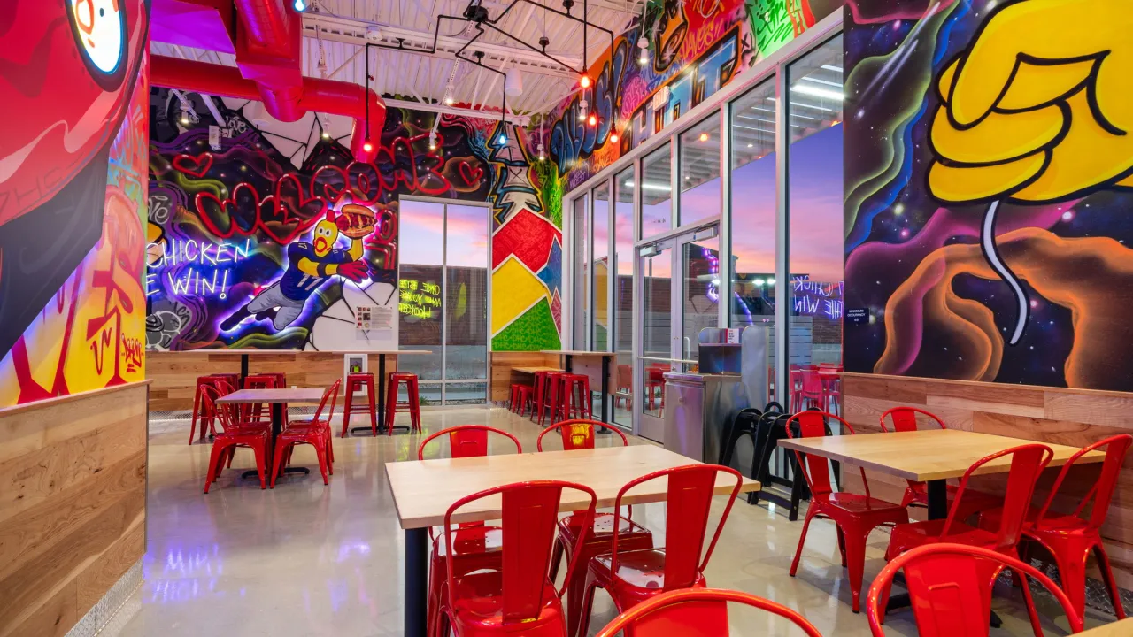 Interior view of Dave's Hot Chicken at 4182 W. 13400 S., Riverton, UT, featuring colorful murals and red seating.