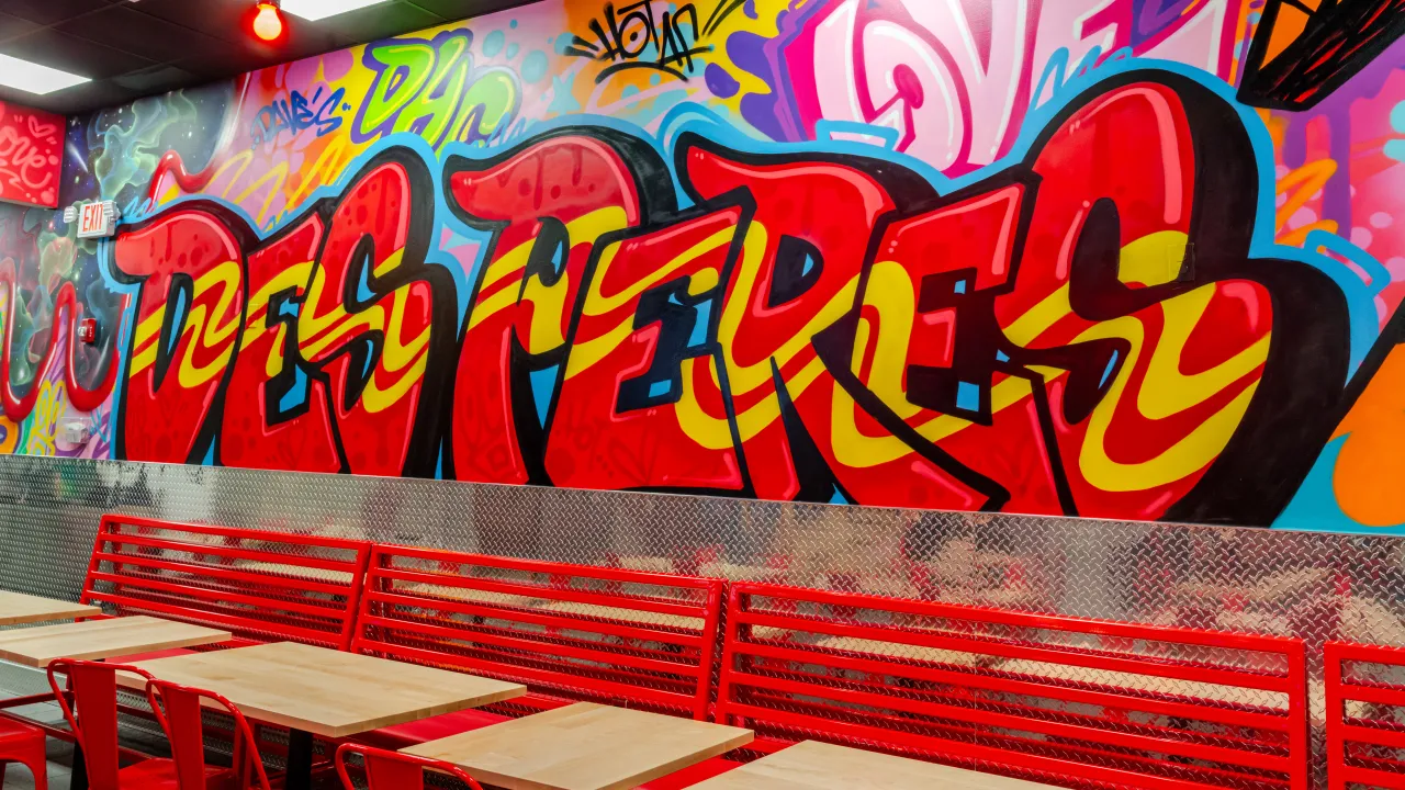 Interior view of Dave's Hot Chicken at 1052 N. Ballas Rd, Des Peres, MO, showcasing vibrant graffiti and red seating.