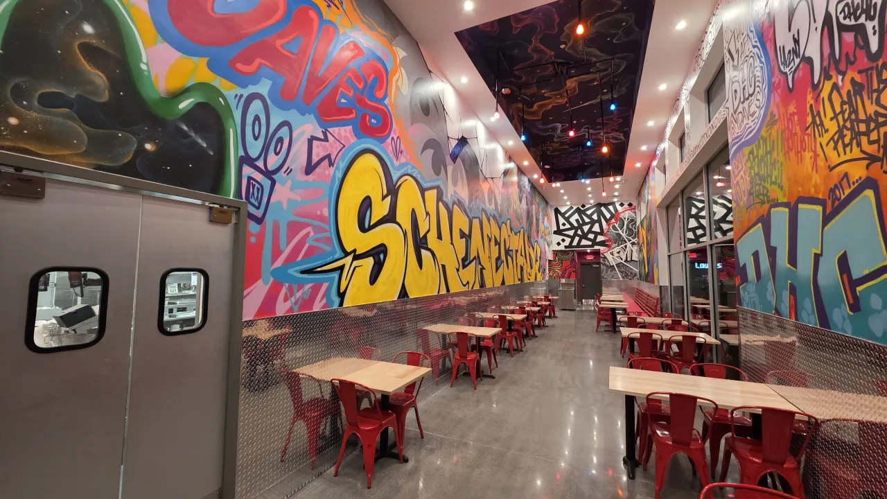 Interior view of Dave’s Hot Chicken on Balltown Rd, Schenectady, NY, showcasing vibrant graffiti art and red seating.
