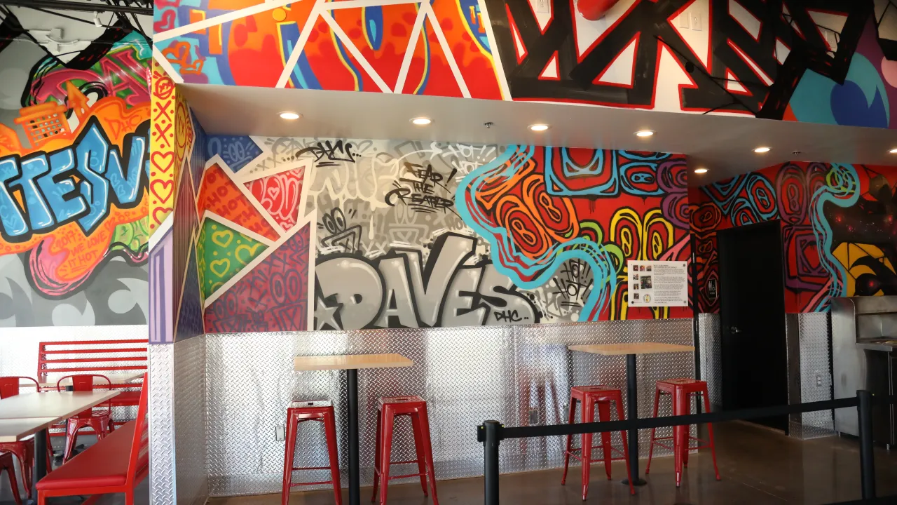 Interior view of Dave's Hot Chicken in Charlottesville, VA, showcasing vibrant murals and red metal seating.