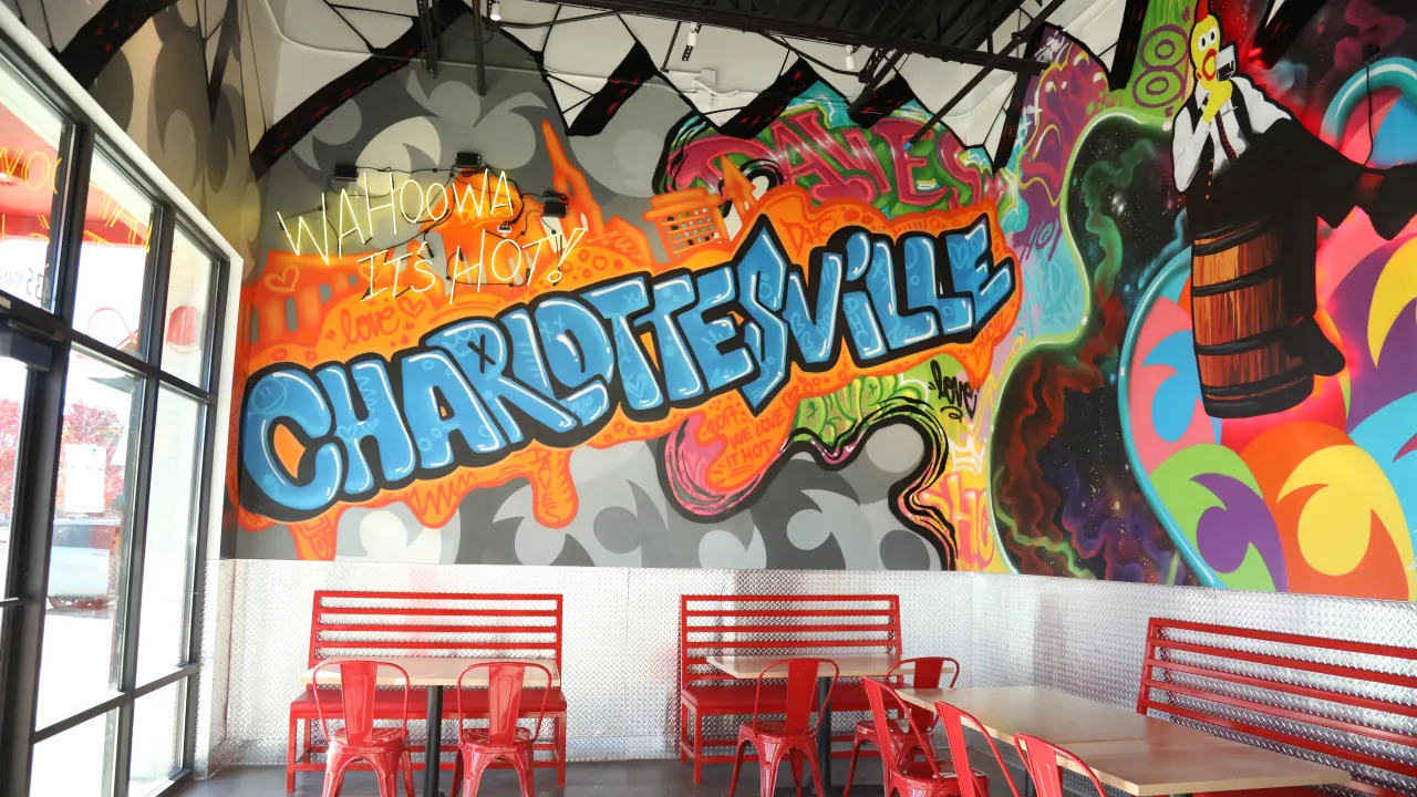 Interior view of Dave's Hot Chicken at 435 Merchant Walk Square, Charlottesville, VA, featuring vibrant murals and red seating.